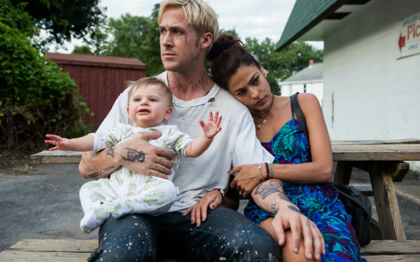Ryan Gosling and Eva Mendes as Luke and Romina from The Place Beyond The Pines sit close on a bench outdoors with a baby in Luke's arms in this 4K Ultra HD movie wallpaper.