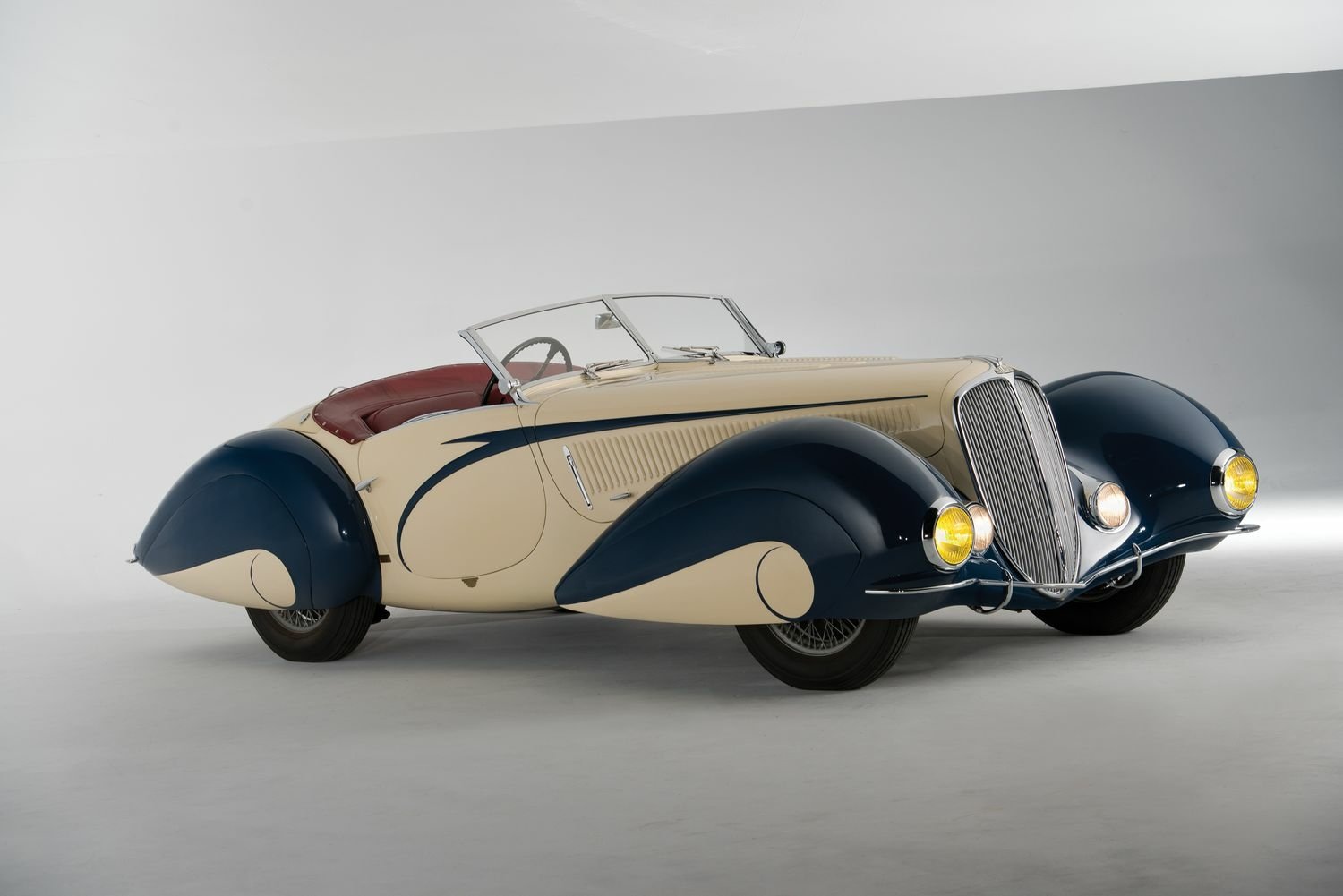 HD PC desktop wallpaper of a Delahaye 135 classic vehicle, a cream-and-navy convertible shown in studio lighting.