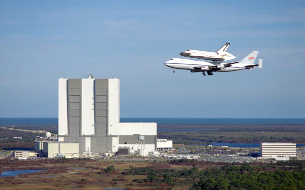 Space shuttle atop a carrier aircraft flying over a coastal launch complex — 2K Quad HD PC desktop wallpaper background showcasing a vehicle and shuttle.