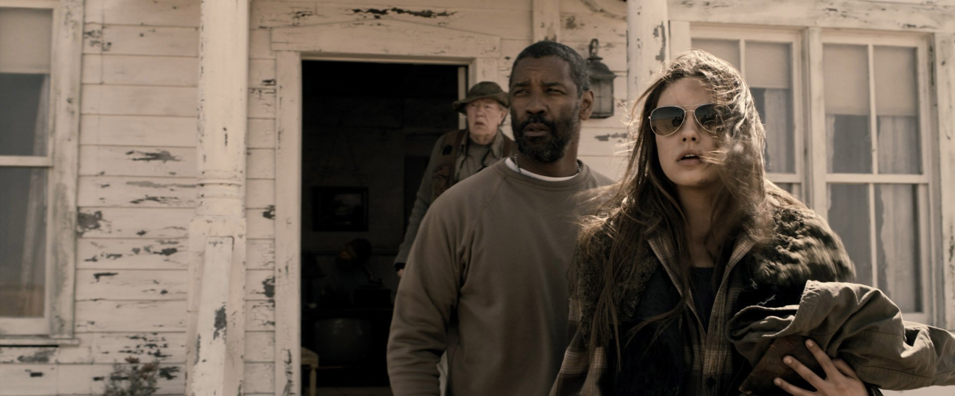 HD PC wallpaper featuring two actors from the movie The Book of Eli: a rugged man and a woman in sunglasses at a weathered porch in a post‑apocalyptic setting.