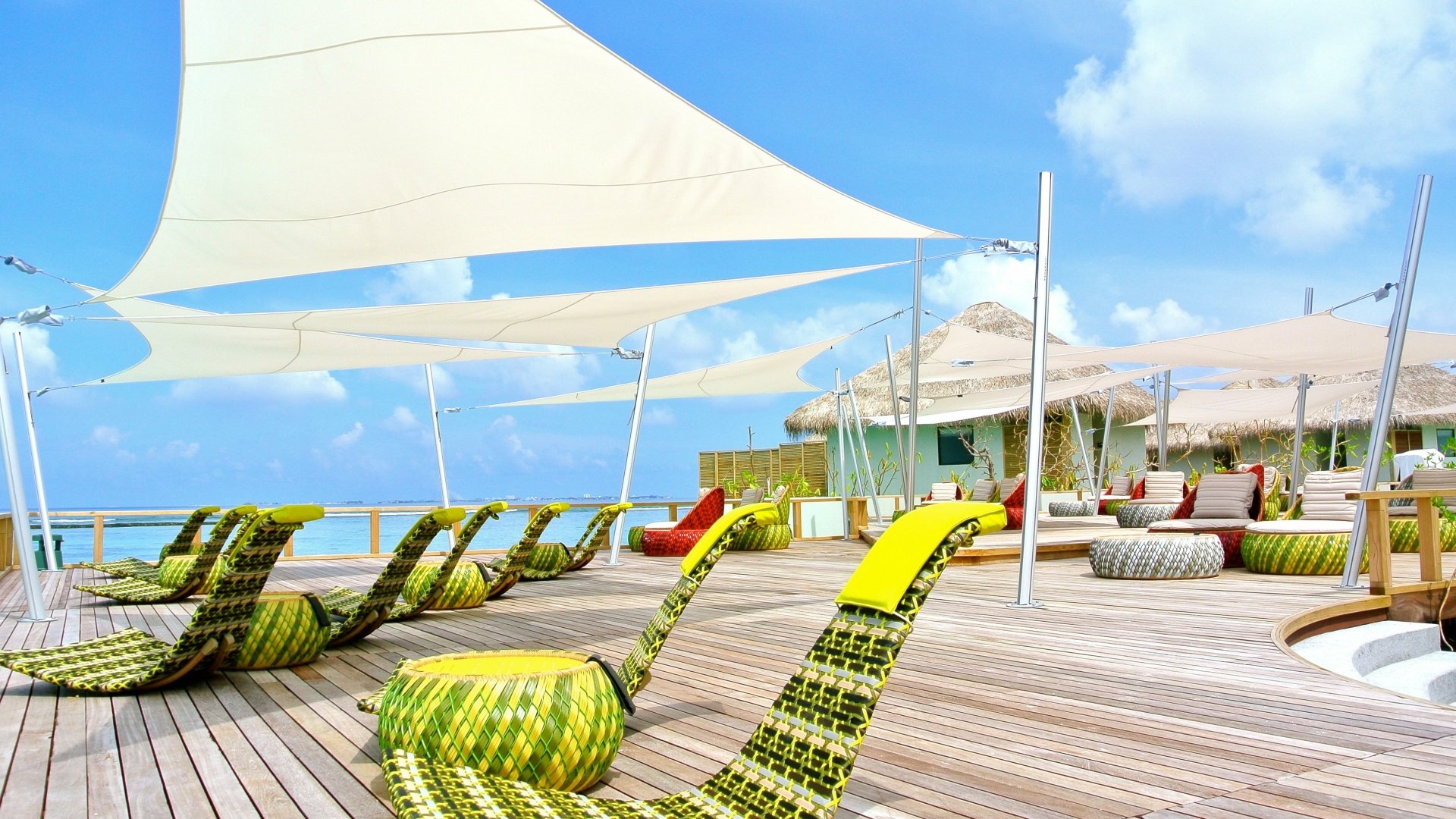 4K Ultra HD desktop wallpaper featuring a vibrant Maldives resort with colorful lounge chairs, sail-like shades, and a bright holiday atmosphere by the ocean.