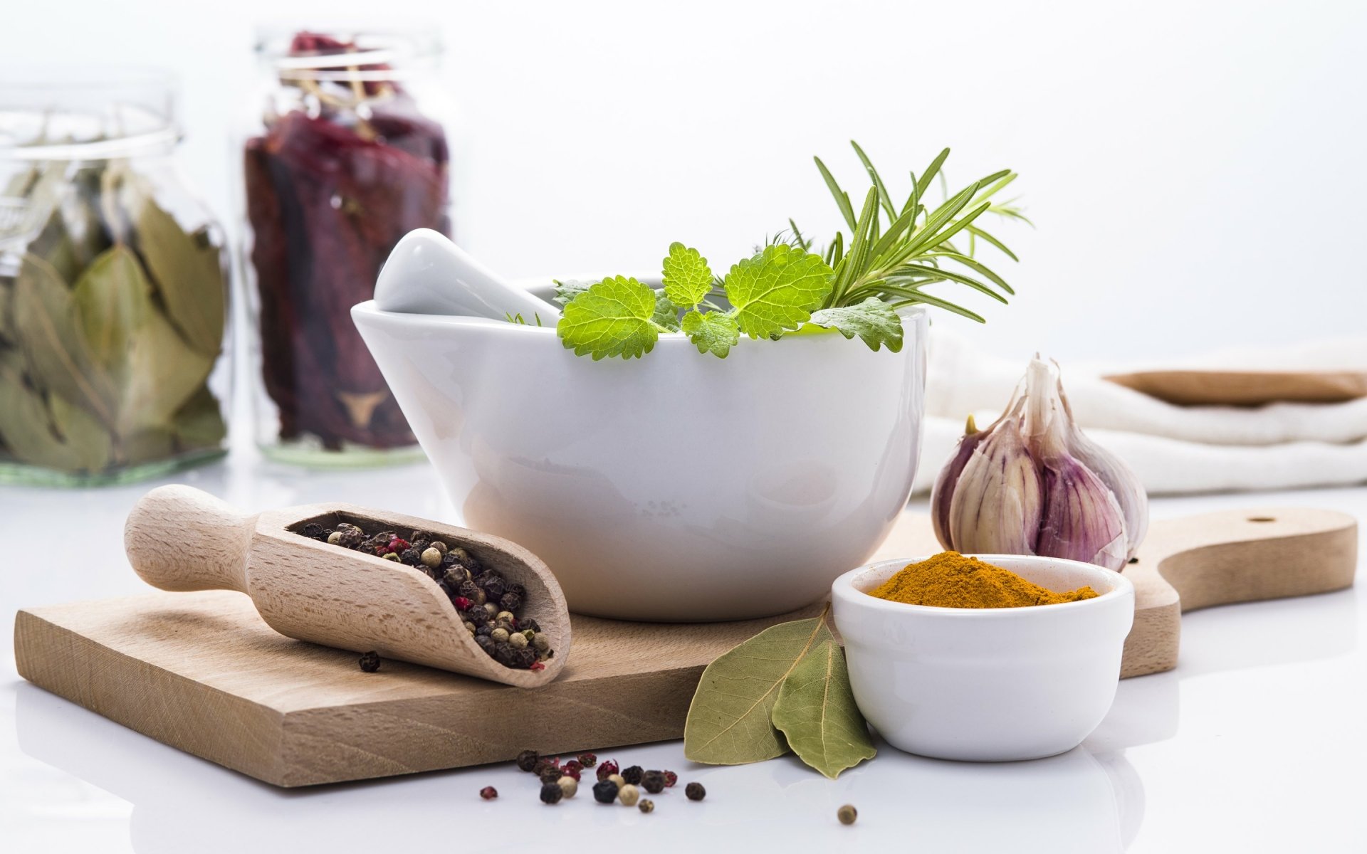 HD desktop wallpaper featuring turmeric powder, garlic, peppercorns, fresh herbs, and bay leaves arranged in a clean still life composition.