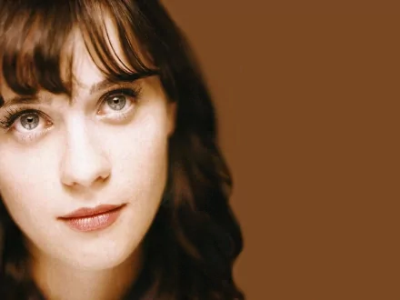 A close-up of Zooey Deschanel, featuring her captivating eyes and soft features against a warm brown background, designed for a stylish HD desktop wallpaper.