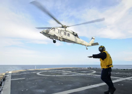 Sikorsky SH-60 Seahawk helicopter hovers above a navy ship deck while a deck crewman signals — HD PC desktop wallpaper background of military aircraft at sea.