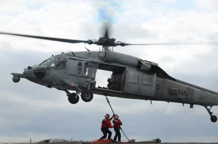 A Sikorsky SH-60 Seahawk Navy military helicopter hovers midair with crew members operating a rescue hoist, captured in 4K Ultra HD quality.