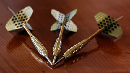 Close-up of brass darts arranged on a wooden surface, showcasing the intricate design of the flights. A striking 4K Ultra HD desktop wallpaper featuring man-made darts.