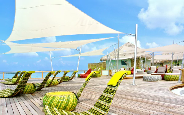 4K Ultra HD desktop wallpaper featuring a vibrant Maldives resort with colorful lounge chairs, sail-like shades, and a bright holiday atmosphere by the ocean.
