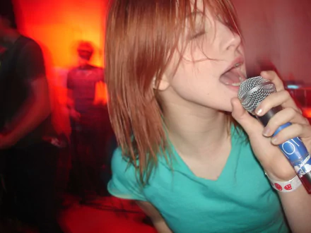 HD desktop wallpaper: close-up of a red-haired female singer gripping a microphone amid blurred orange stage lights, conveying an energetic live music performance.