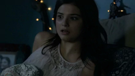 Stefanie Scott in a tense moment from Insidious: Chapter 3, featuring a dark bedroom setting illuminated by soft lights, capturing the movie's eerie atmosphere.