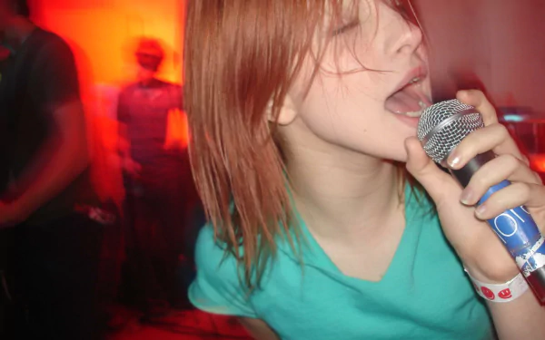 HD desktop wallpaper: close-up of a red-haired female singer gripping a microphone amid blurred orange stage lights, conveying an energetic live music performance.