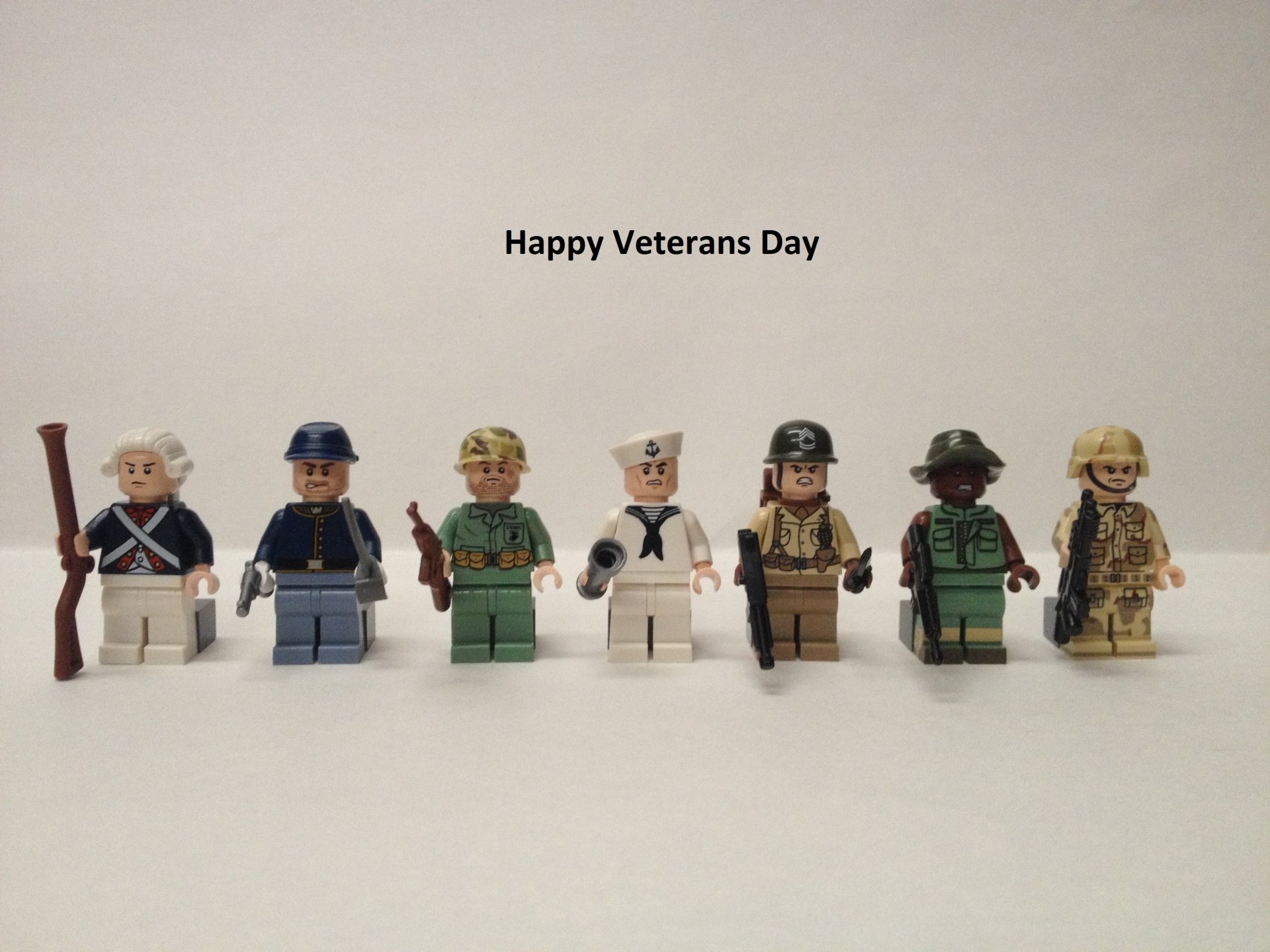 HD PC desktop wallpaper featuring seven LEGO figures dressed in various military uniforms with the text Happy Veterans Day above, commemorating the holiday.