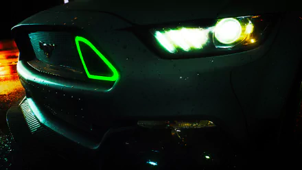 Close-up of a Mustang's front headlight with glowing green accents from the video game Need For Speed (2015), displayed as an HD PC desktop wallpaper.