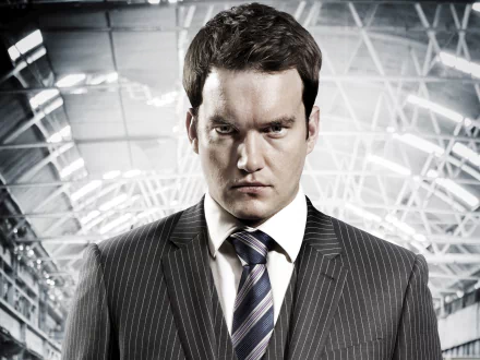 HD PC desktop wallpaper featuring a serious man in a suit from the TV show Torchwood, set against a bright, industrial-style background.
