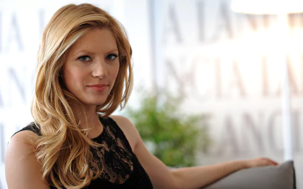 HD desktop wallpaper featuring celebrity Katheryn Winnick with blonde hair, wearing a black lace top, seated against a softly blurred background.