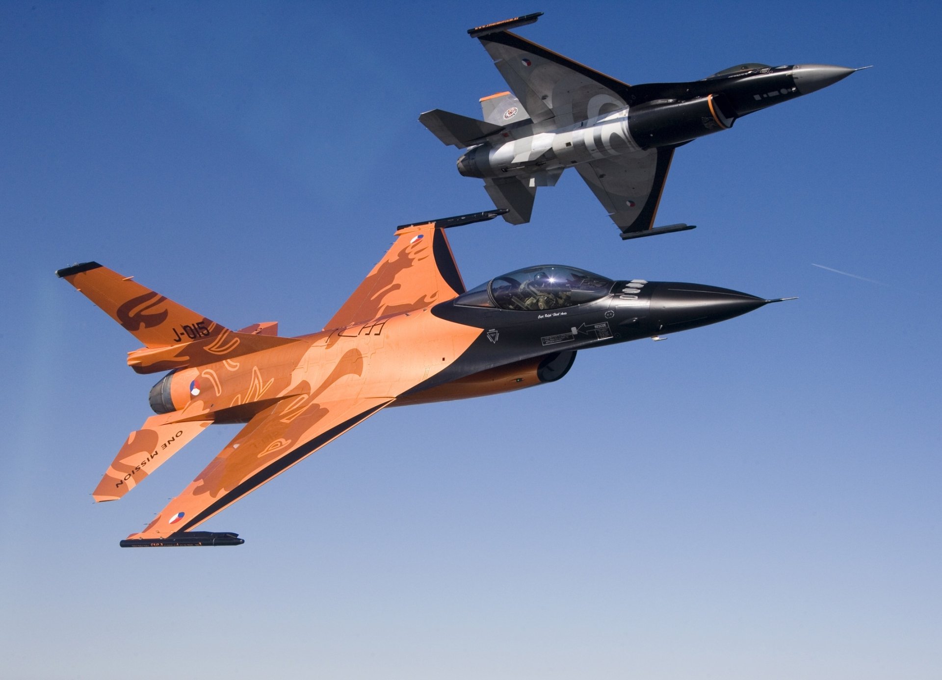 HD PC desktop wallpaper of two General Dynamics F-16 Fighting Falcon jets — orange-and-black and gray — flying in close formation against a clear blue sky (military aircraft).