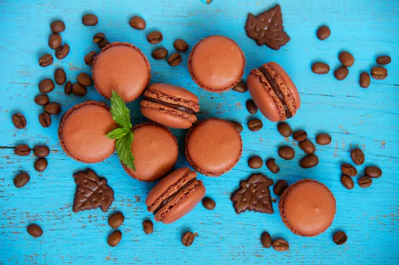 Close-up of chocolate macarons and coffee beans scattered on a bright blue wooden surface, with pieces of chocolate and a sprig of mint, in vibrant 4K Ultra HD detail.