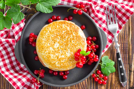 Stack of golden pancakes garnished with fresh red currants on a black plate, set on a red and white checkered cloth, captured in 4K Ultra HD for PC wallpaper and background.
