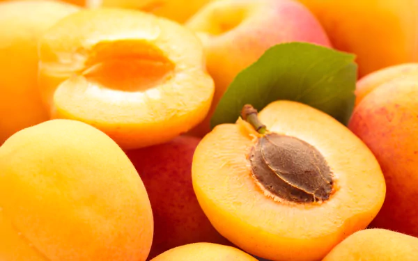 Close-up of ripe apricots with one halved to reveal the seed, captured in vibrant detail as a 4K Ultra HD PC desktop wallpaper background.