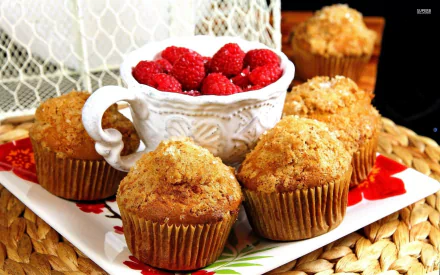 A vibrant HD desktop wallpaper featuring golden muffins on a floral plate, accompanied by a white bowl of fresh raspberries, adding a touch of sweetness to the scene.