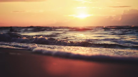 HD desktop wallpaper showcasing a tranquil beach scene with gentle waves and a warm, glowing sunset over the horizon.