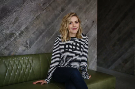 HD PC desktop wallpaper of celebrity Kiernan Shipka sitting on a green leather bench against a textured gray wall, wearing a black-and-white striped sweater.