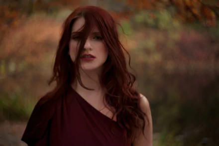 A redhead woman with flowing hair stands against a soft bokeh background, exuding a captivating presence. This 4K Ultra HD image serves as a stunning PC desktop wallpaper.