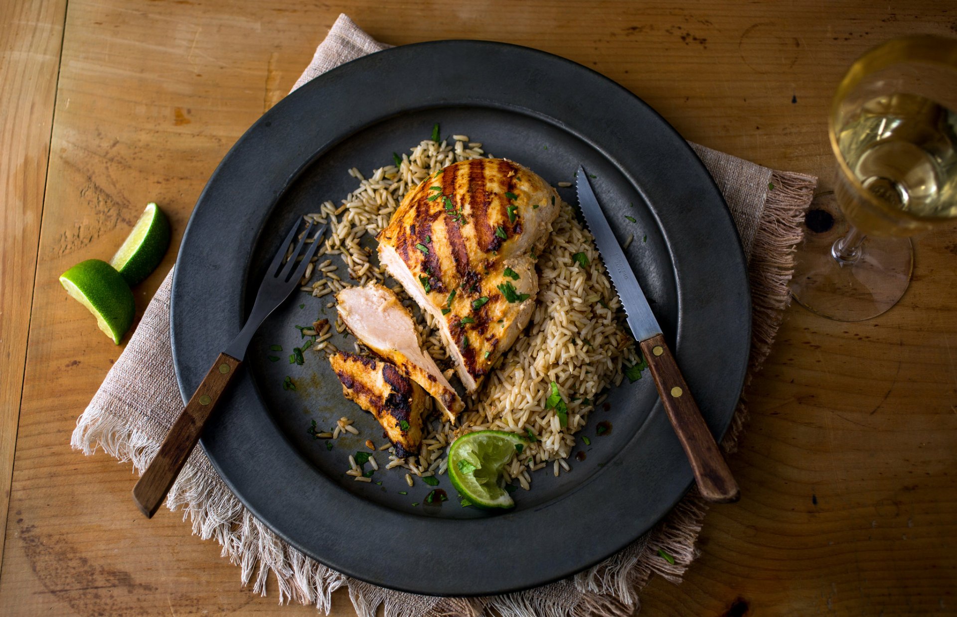 A HD PC desktop wallpaper showing a diner-style meal of grilled chicken breast served on a bed of seasoned rice with a lime wedge, accompanied by cutlery and a drink.