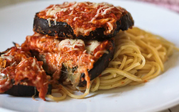 Close-up of baked eggplant Parmesan over a bed of spaghetti, captured in stunning 4K Ultra HD as a PC desktop wallpaper and background.