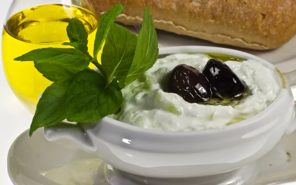 4K Ultra HD PC desktop wallpaper: close-up of creamy tzatziki in a bowl topped with olives and olive oil, garnished with fresh mint, with bread in the background.