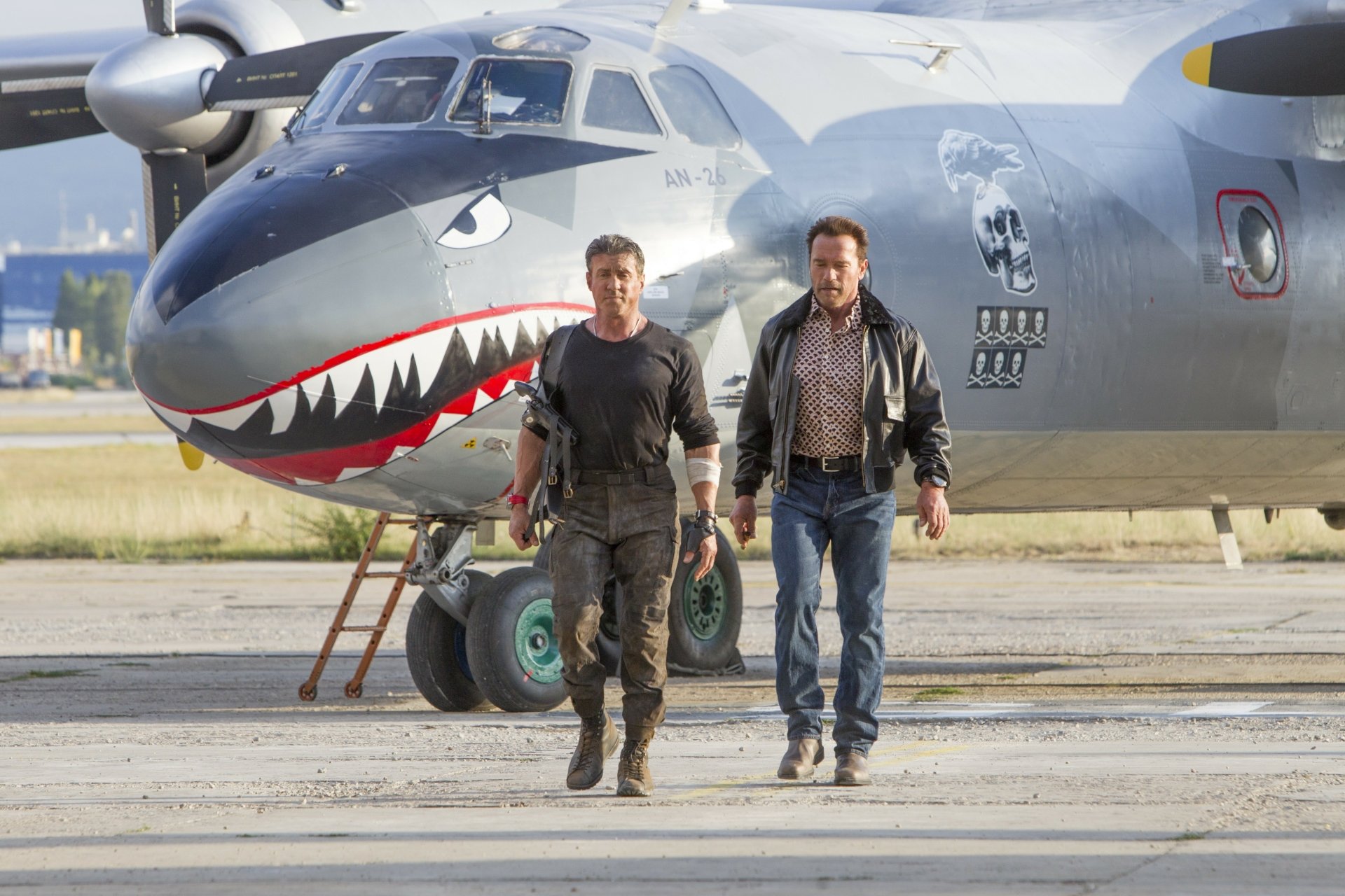 Arnold Schwarzenegger and Sylvester Stallone as Barney Ross in a scene from The Expendables 3, walking on the tarmac beside a military aircraft.