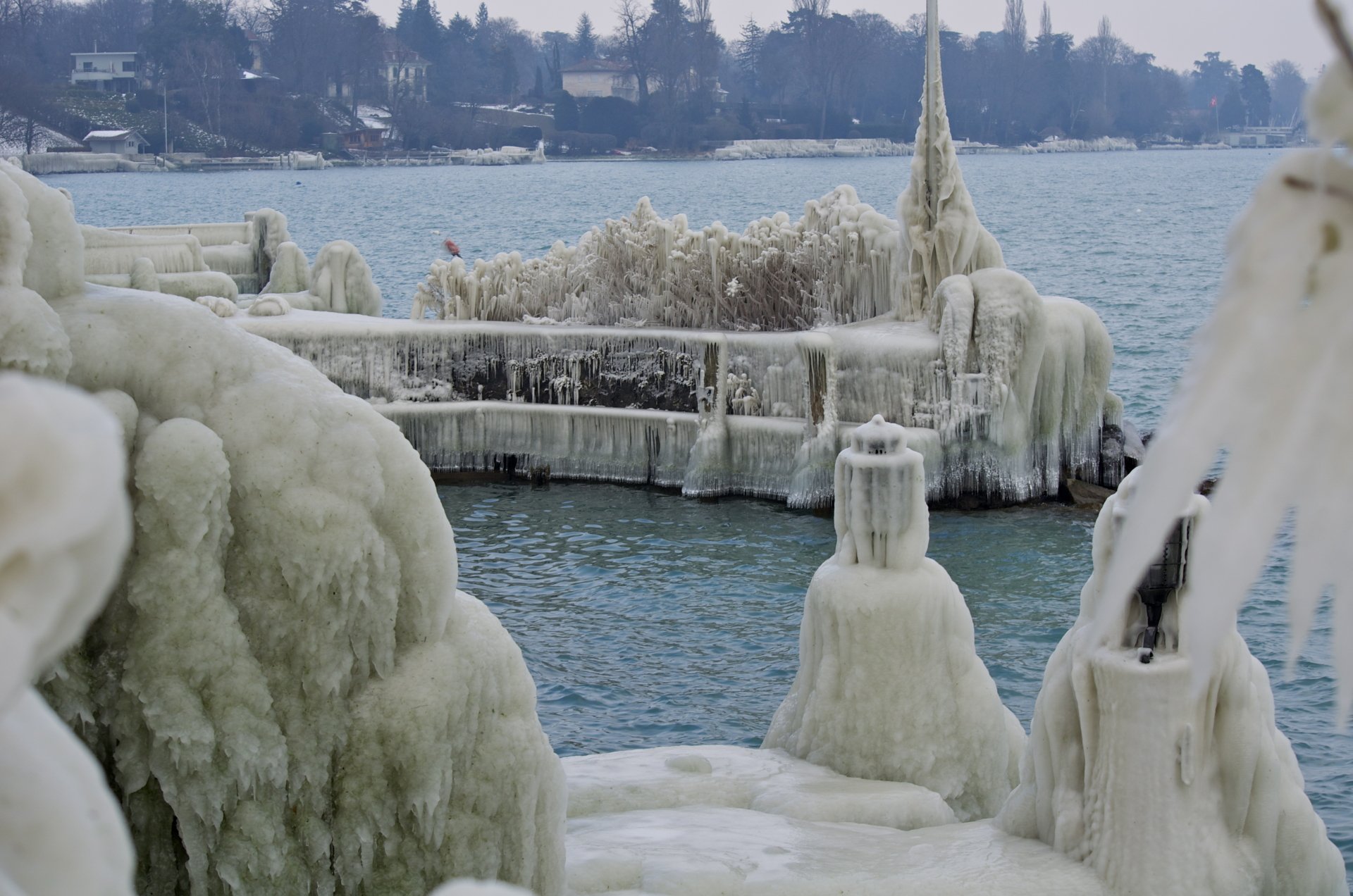 4K Ultra HD PC Desktop Wallpaper and Background — icy lakeshore with sculpted ice draping a pier and railings, frozen formations rising above calm blue water and a distant frosted shoreline.
