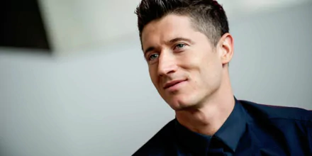 HD wallpaper featuring Polish soccer player Robert Lewandowski with a confident smile, dressed in a stylish outfit. The background is simple and blurred to highlight the athlete.