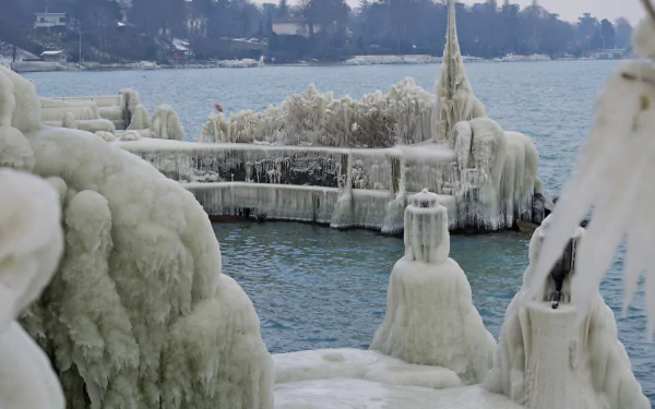 4K Ultra HD PC Desktop Wallpaper and Background — icy lakeshore with sculpted ice draping a pier and railings, frozen formations rising above calm blue water and a distant frosted shoreline.