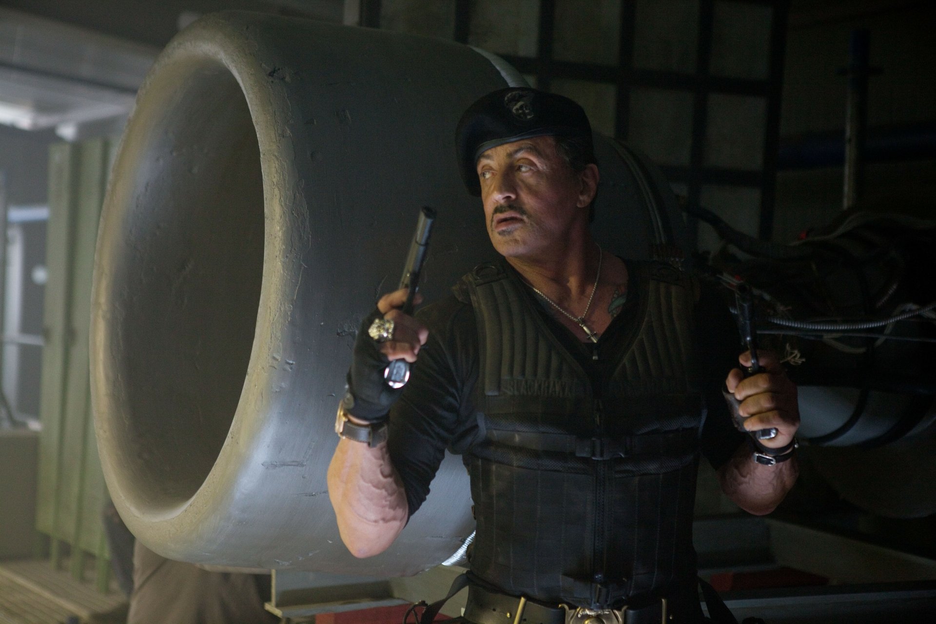 Battle-hardened action hero in tactical vest and cap, dual-wielding pistols beside a jet engine — cinematic still from an action movie, 5K Ultra HD PC desktop wallpaper.