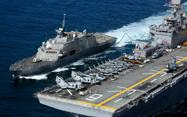 USS Freedom (LCS-1) littoral combat ship alongside an aircraft carrier flight deck with helicopters; USS Cape Gloucester (AKV-9) markings — United States Navy military 4K wallpaper.
