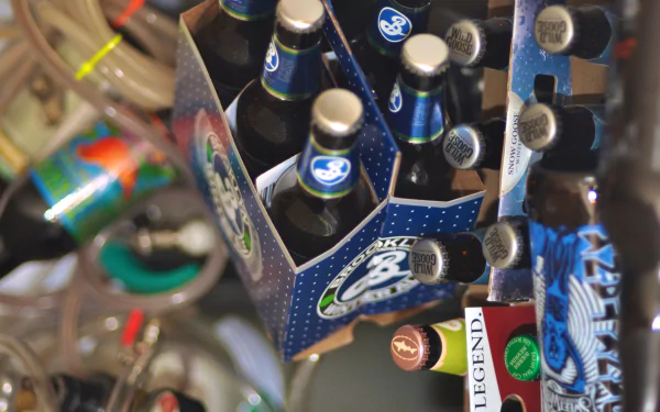 4K Ultra HD wallpaper featuring a close-up of a six-pack of bottled beer surrounded by various food and drink items on a cluttered surface.