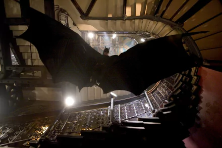 HD wallpaper featuring a scene from the movie Batman Begins, showing Batman gliding in a dark, industrial staircase.