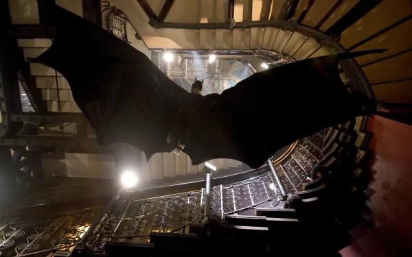 HD wallpaper featuring a scene from the movie Batman Begins, showing Batman gliding in a dark, industrial staircase.
