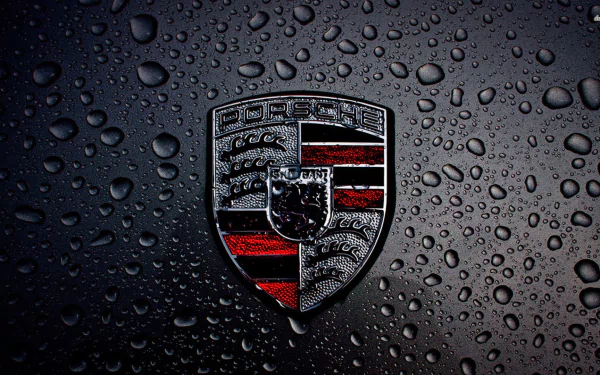 HD desktop wallpaper featuring a close-up of a Porsche emblem on a black surface covered with water droplets.