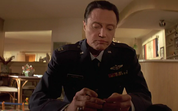 HD PC desktop wallpaper: movie still of an actor in military dress uniform seated at a kitchen table, solemnly handling a small object in a warmly lit living-room setting.