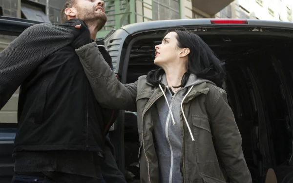 Krysten Ritter as Jessica Jones gripping a man’s collar on a city street, captured in a dynamic scene from the TV show, featured as an HD PC desktop wallpaper.