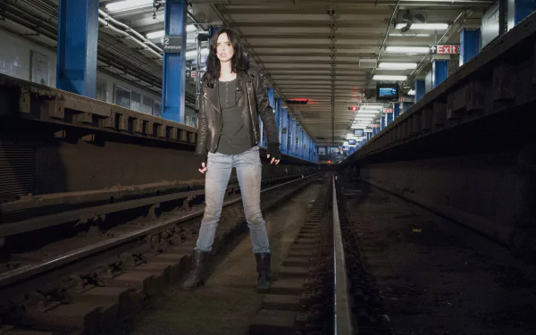 Krysten Ritter as Jessica Jones stands confidently on subway tracks in a dimly lit tunnel, captured in a 4K Ultra HD TV show wallpaper background.
