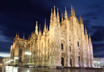 Night view of Milan Cathedral in Italy, illuminated against a deep blue sky, showcasing its intricate religious Gothic architecture in stunning 4K Ultra HD detail.