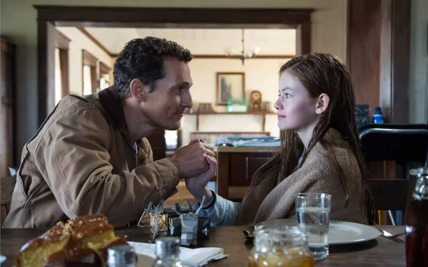 HD PC desktop wallpaper featuring Mackenzie Foy and Matthew McConaughey in a scene from the movie Interstellar, sitting at a dining table and holding hands.