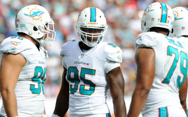HD desktop wallpaper showing three football players in Miami Dolphins uniforms standing together on the field during a game.