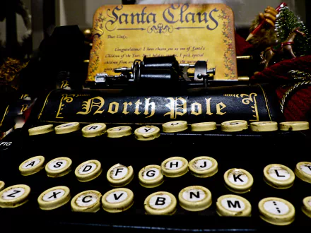 Close-up of a vintage typewriter with North Pole on the roller, surrounded by holiday and Christmas decorations, featured as an HD PC desktop wallpaper.
