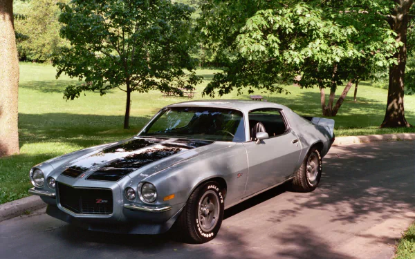 HD desktop wallpaper featuring a classic silver Chevrolet Camaro Z28 parked under trees on a sunny day.