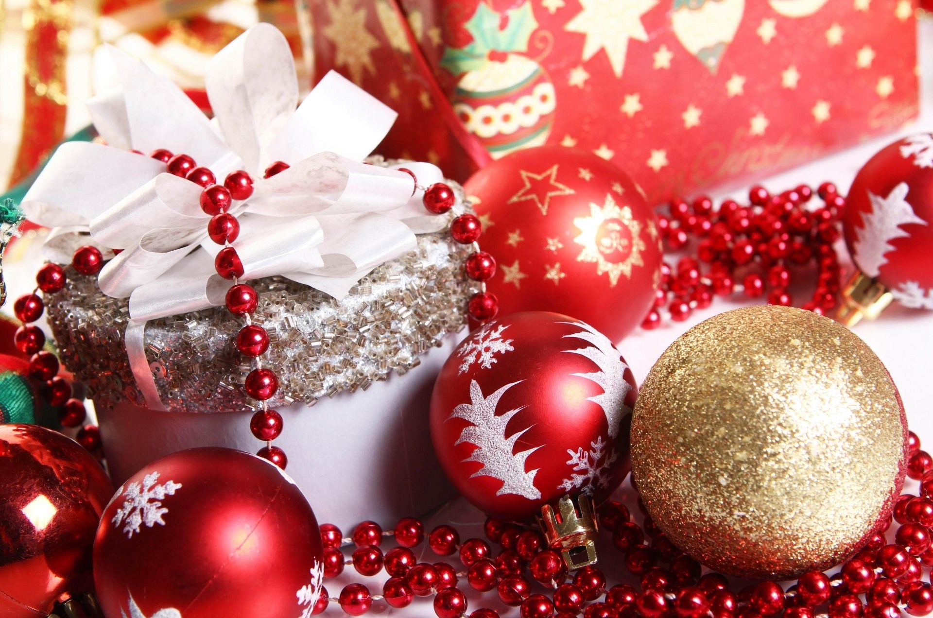 A festive arrangement featuring red and gold Christmas ornaments, a silver gift wrapped with a white ribbon, and red garland, creating a vibrant holiday atmosphere.