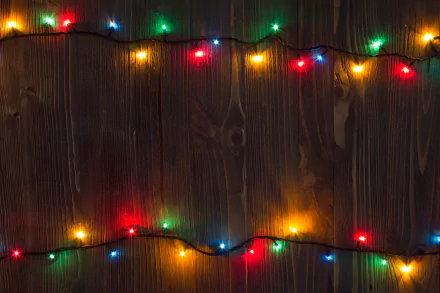HD PC desktop wallpaper featuring colorful Christmas lights glowing against a dark wooden background, capturing a festive holiday atmosphere.