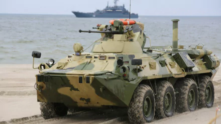 HD military desktop wallpaper featuring a camouflaged BTR-80 armored personnel carrier on a sandy shore with a naval ship in the background.